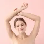 Mulher de olhos fechados, levantando os braços mostrando axilas sem pelos
